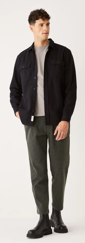 A man wearing a black Frank & Oak button up shirt with dark green pants and black boots