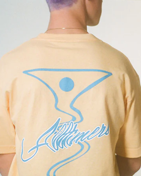 A man wearing a peach and light blue All-timers t-shirt with a martini graphic on it