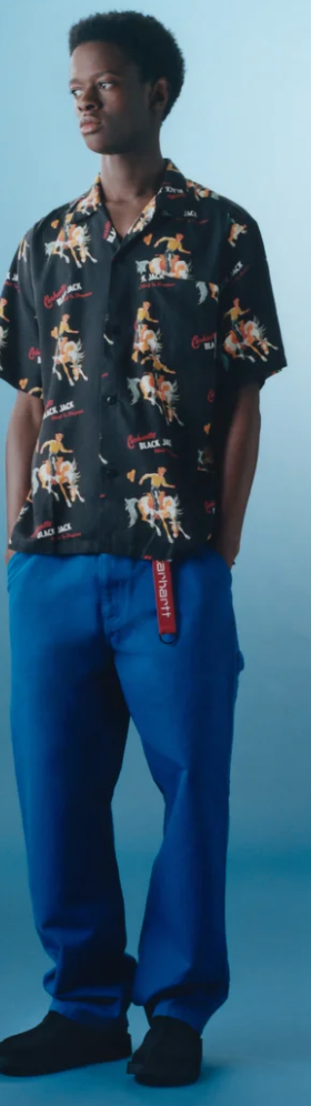 A man wearing a Carhartt WIP black graphic button-up with blue pants and branded carhartt belt