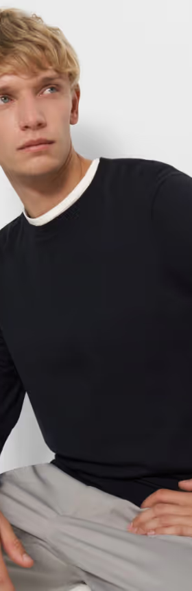 A man sitting down wearing a Theory outfit feating a navy blue sweater and grey pleated pants