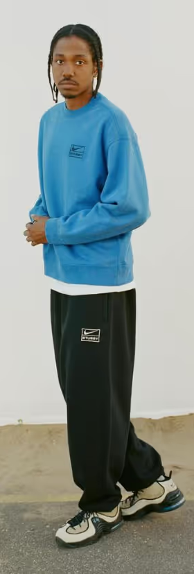 A man walking and wearing a blue Nike sweatshirt and black sweatpants