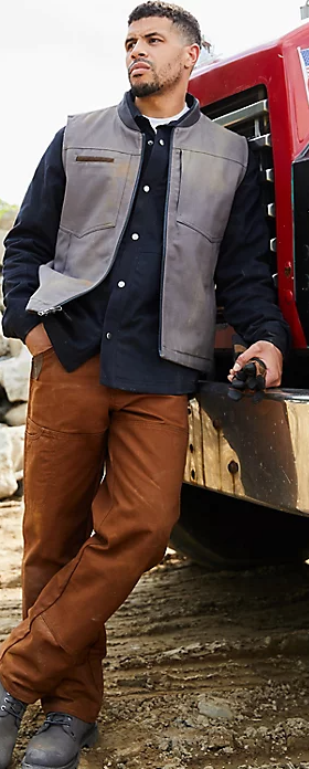 A man wearing a wrangler vest, button up and brown pants