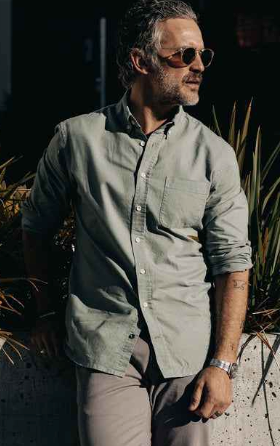 A man wearing a Taylor Stitch olive long-sleeve button up, grey pants and sunglasses