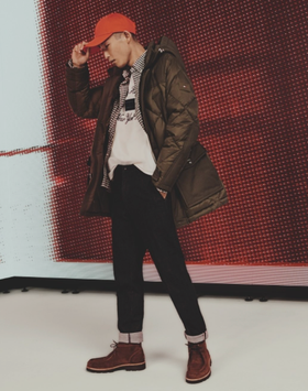 A man wearing a red Tommy Hilfiger hat, brown winter coat and jeans
