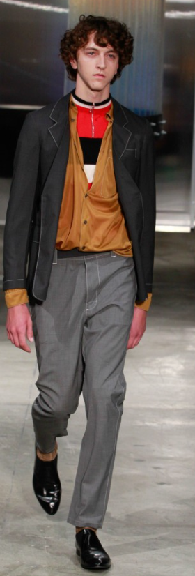 A man wearing a Prada outfit with grey pants and a brown cardigan