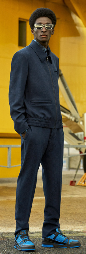 A man wearing a slick Louis Vuitton suit with blue high-top sneakers and gold sunglasses