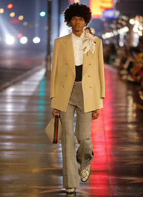 A man wearing a Gucci brown coat and checkered pants with snake skin boots