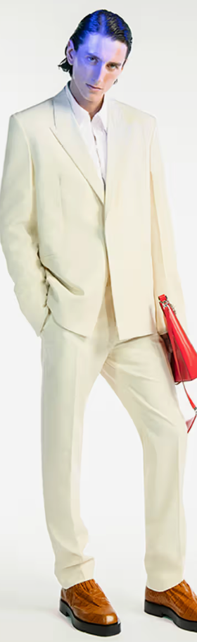 A man wearing a cream Givenchy suit with a red bag and brown shoes