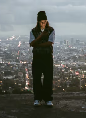 A man standing on a mountain above the city wearing a Polar Skate Co. Sweater and Pants