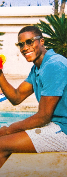 A man sitting by a pool in Ted Baker swimshorts and a blue polo