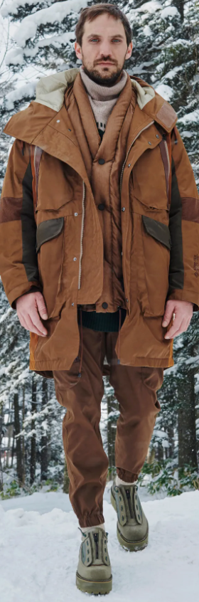 A man wearing a layered brown White Mountaineering outfit with two brown jackets and matching brown pants