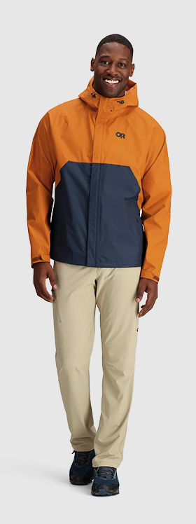 A man wearing an orange and navy blue Outdoor Research Jacket and beige pants