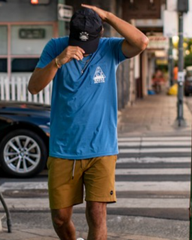 A man wearing a bright blue RVCA t-shirt, blue hat and brown bathing suit