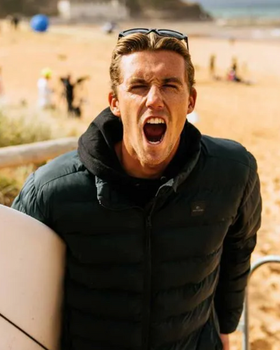 A man wearing a a Rip Curl hoodie and jacket holding a surf board