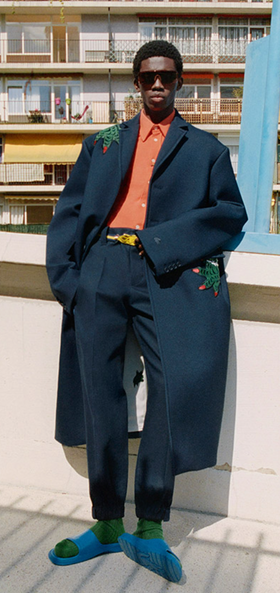 A man wearing a fashionable lacoste suit with flower embroidery on it and blue sandals
