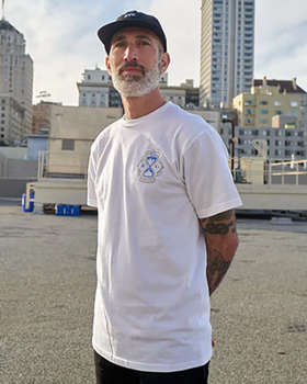 A man standing wearing a Benny Gold white t-shirt and black hat