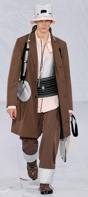 A man walking a runway in a Craig Green designer construction-influenced brown outfit with an overcoat and wide pants