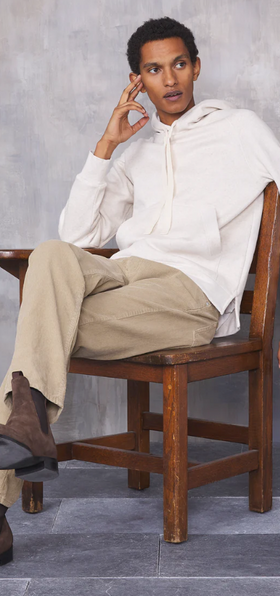 A man sitting in a chair wearing a minamilist Officine Generale white hoodie and khaki pants along with brown boots
