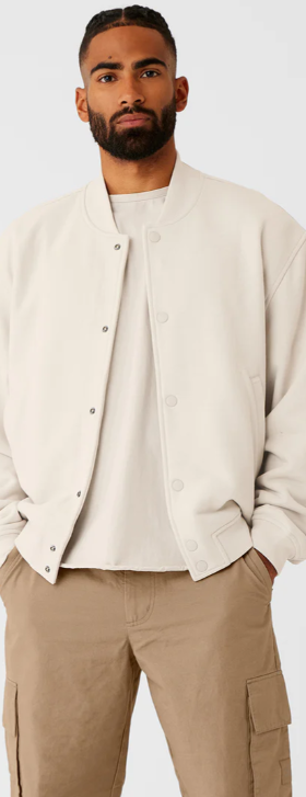 A man wearing a cream Alo bomber jacket and brown pants