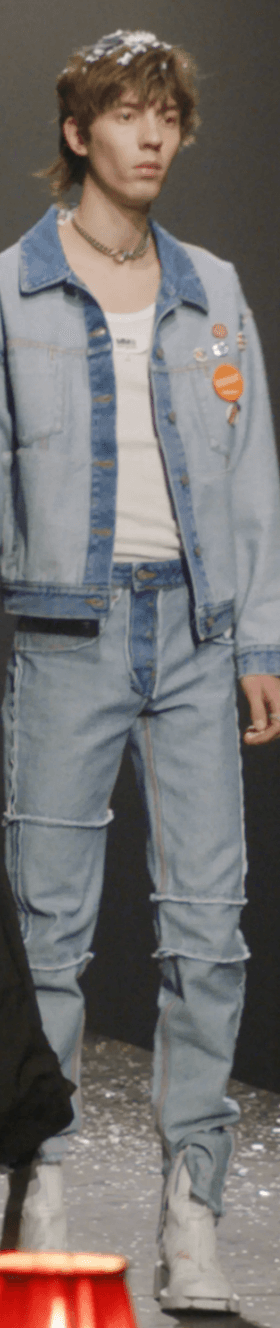 A man on a fashion runway wearing a Maison Margiela denim jacket and matching pants along with a white high-heel boots
