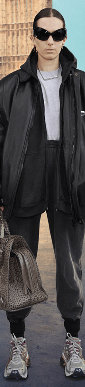 A person wearing a Balenciaga black leather sports coat, dark grey sweats, white sneakers and oversize sunglasses