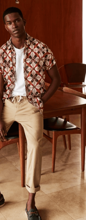A man wearing a patterned J Crew short-sleeve button up with rolled up beige khakis and boat shoes