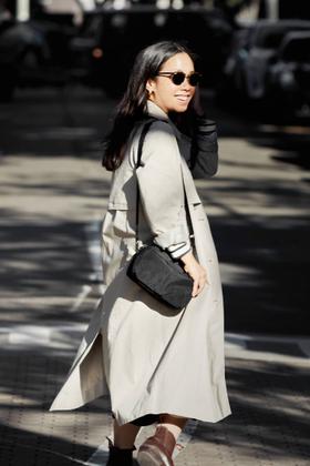 A woman wearing a beige trench coat with a black Bellroy crossbody bag