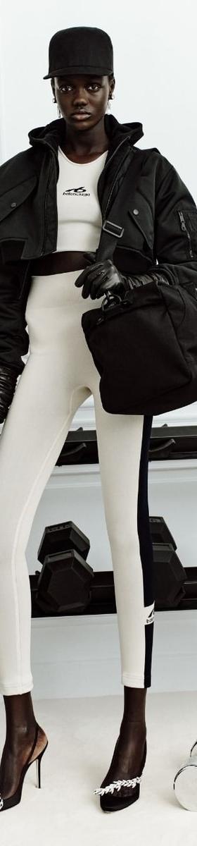 A woman wearing crystal-buckled Manolo Blahnik pumps with white leggings and a black bomber jacket